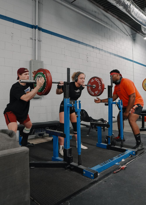 Female powerlifter squatting with side spotters